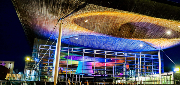 The Senedd building lit up in the colours of a rainbow.