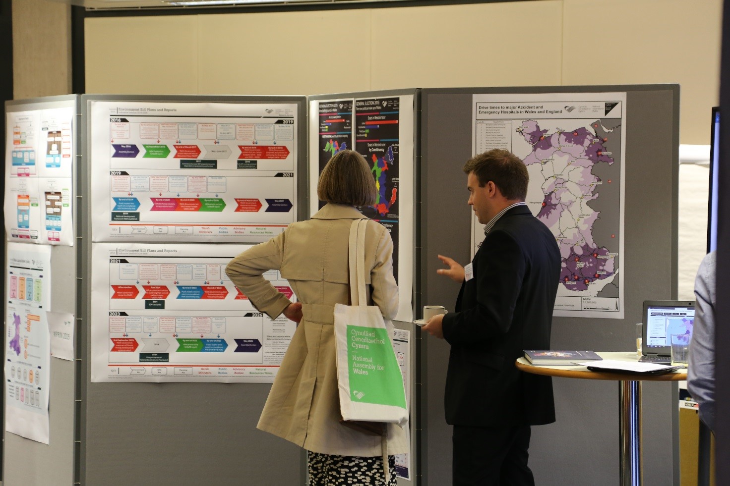 Image of a man and woman discussing maps and diagrams that have been pinned on a wall